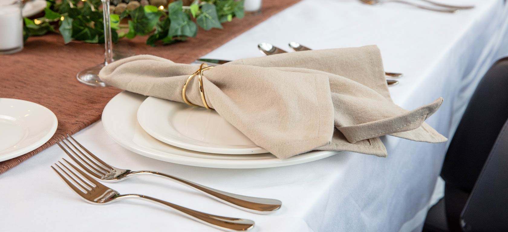 Elegant beige cloth napkin in golden napkin ring sitting on ornate table.