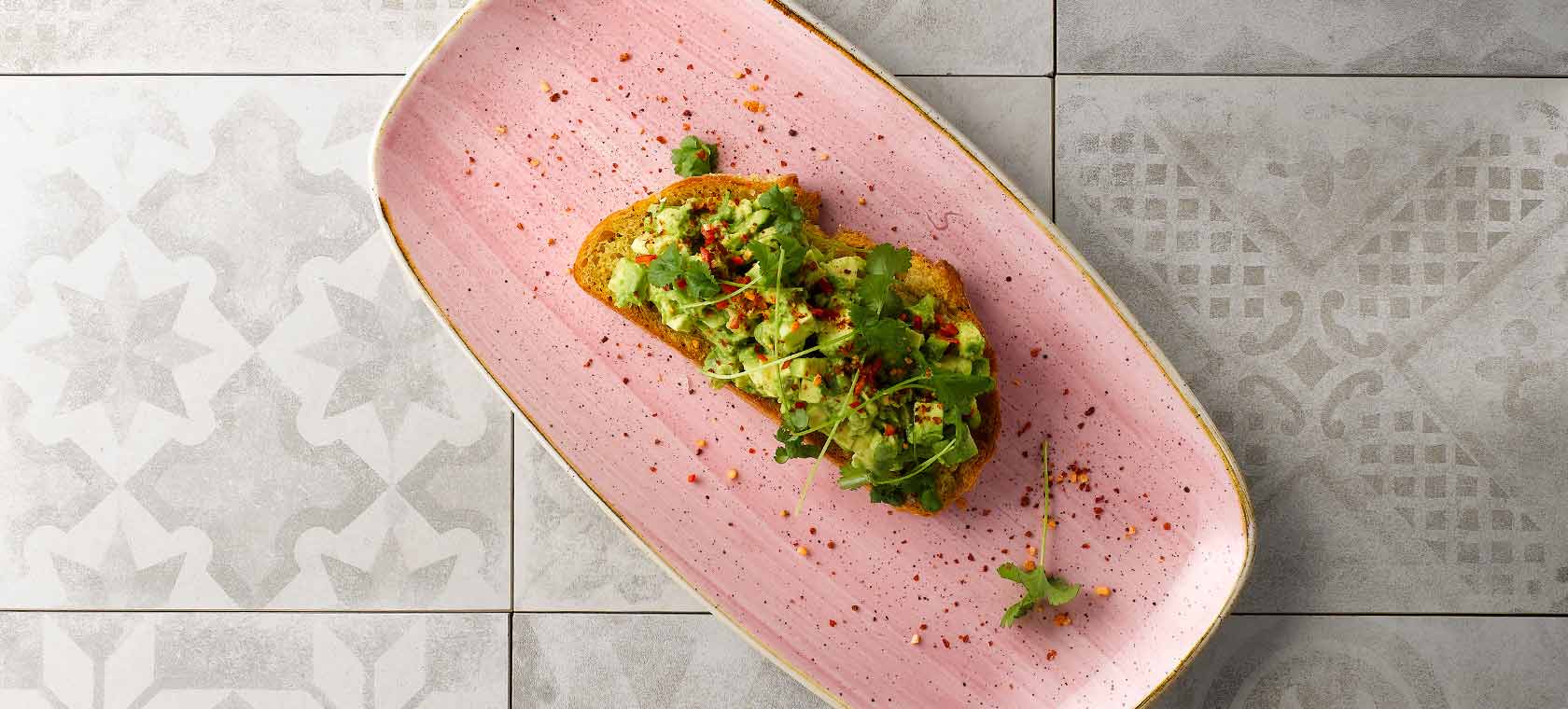 Long flat pink dish holding avocado toast a garnished with parsley.