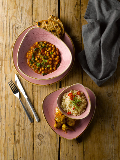 Blush-toned asymmetrical plates and bowls containing a Mediterranean meal.