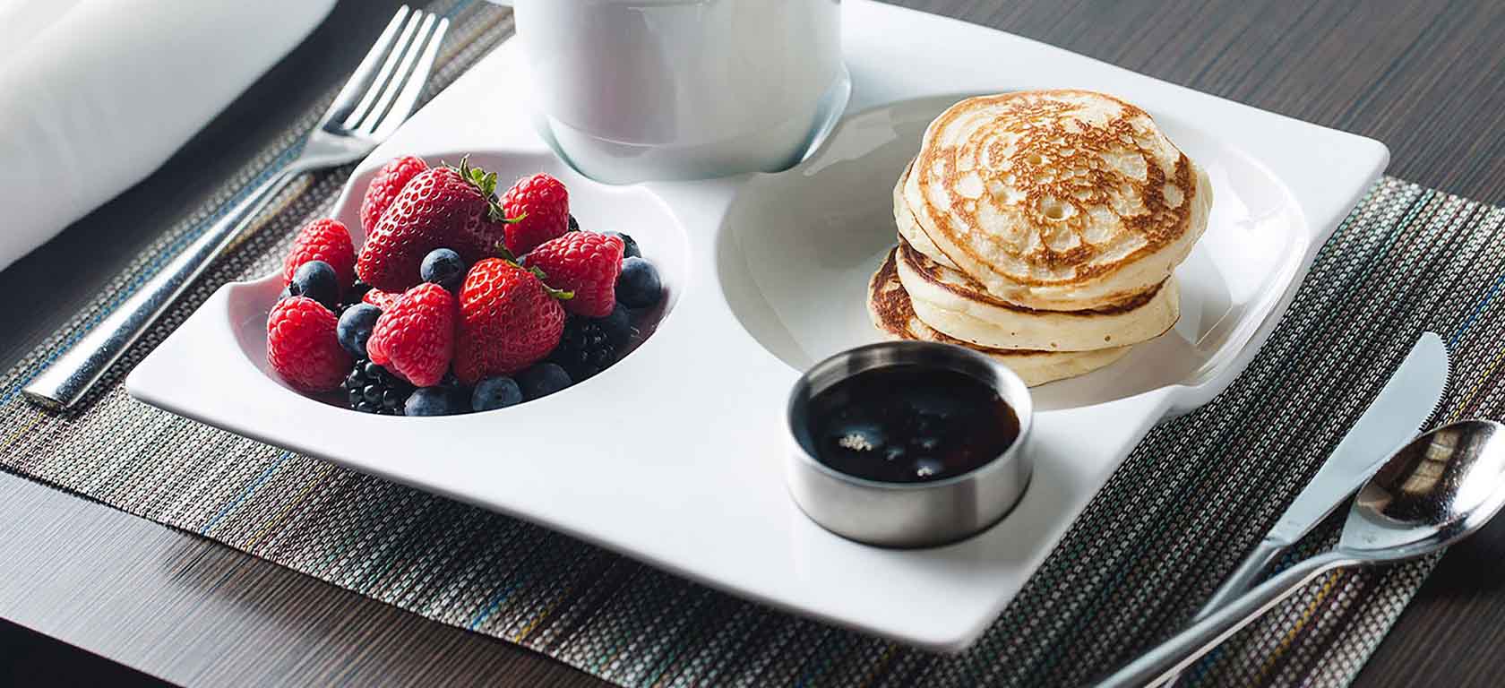 Intricate undulated white ceramic dish holding a pancakes and fruit breakfast.