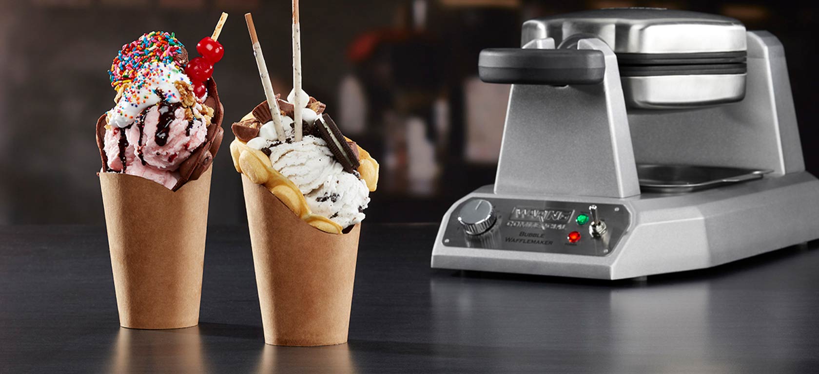 Silver Waring waffle maker in the background with two appetizing waffle ice-cram cones in the front.